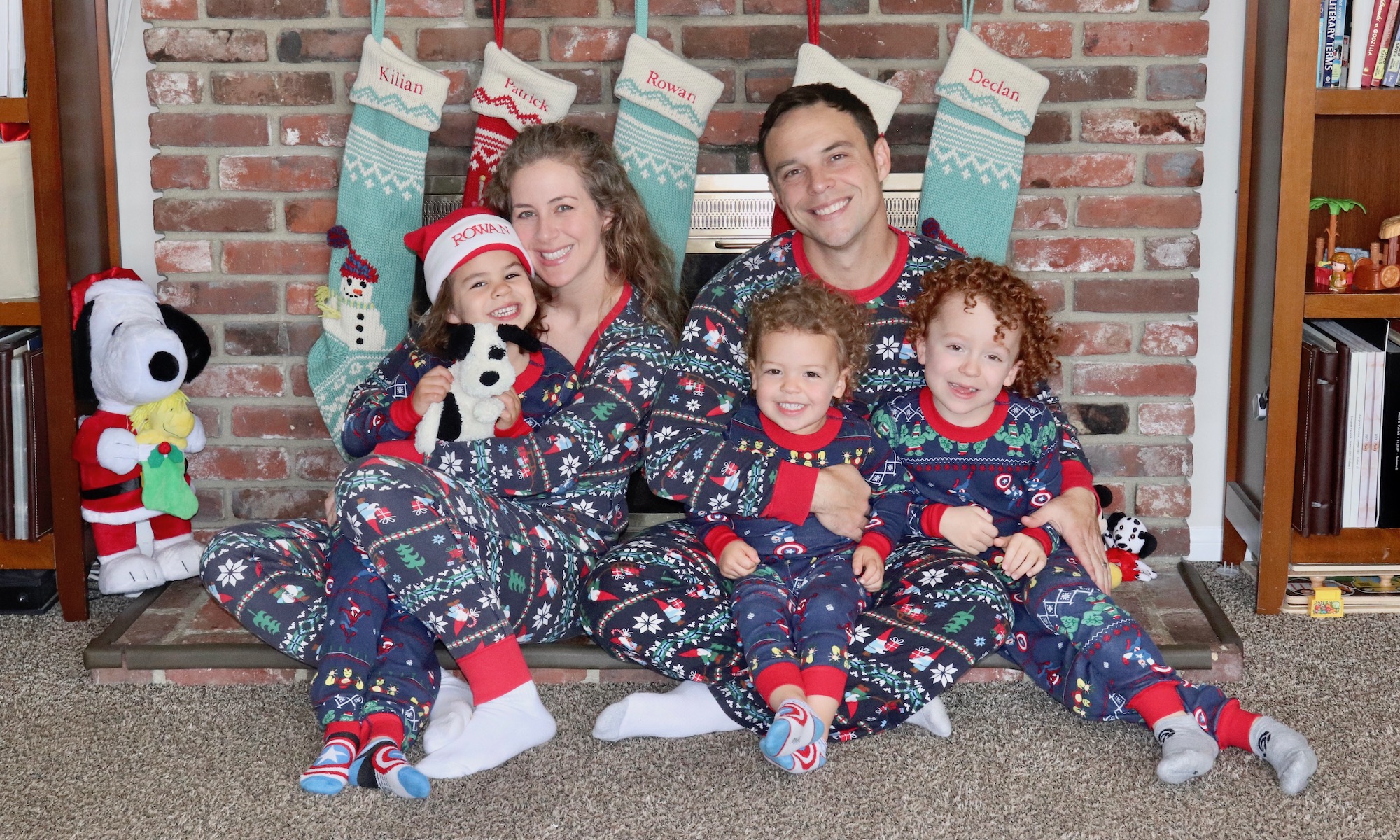 A family wearing Christmas pajamas sitting in front of a fireplace.